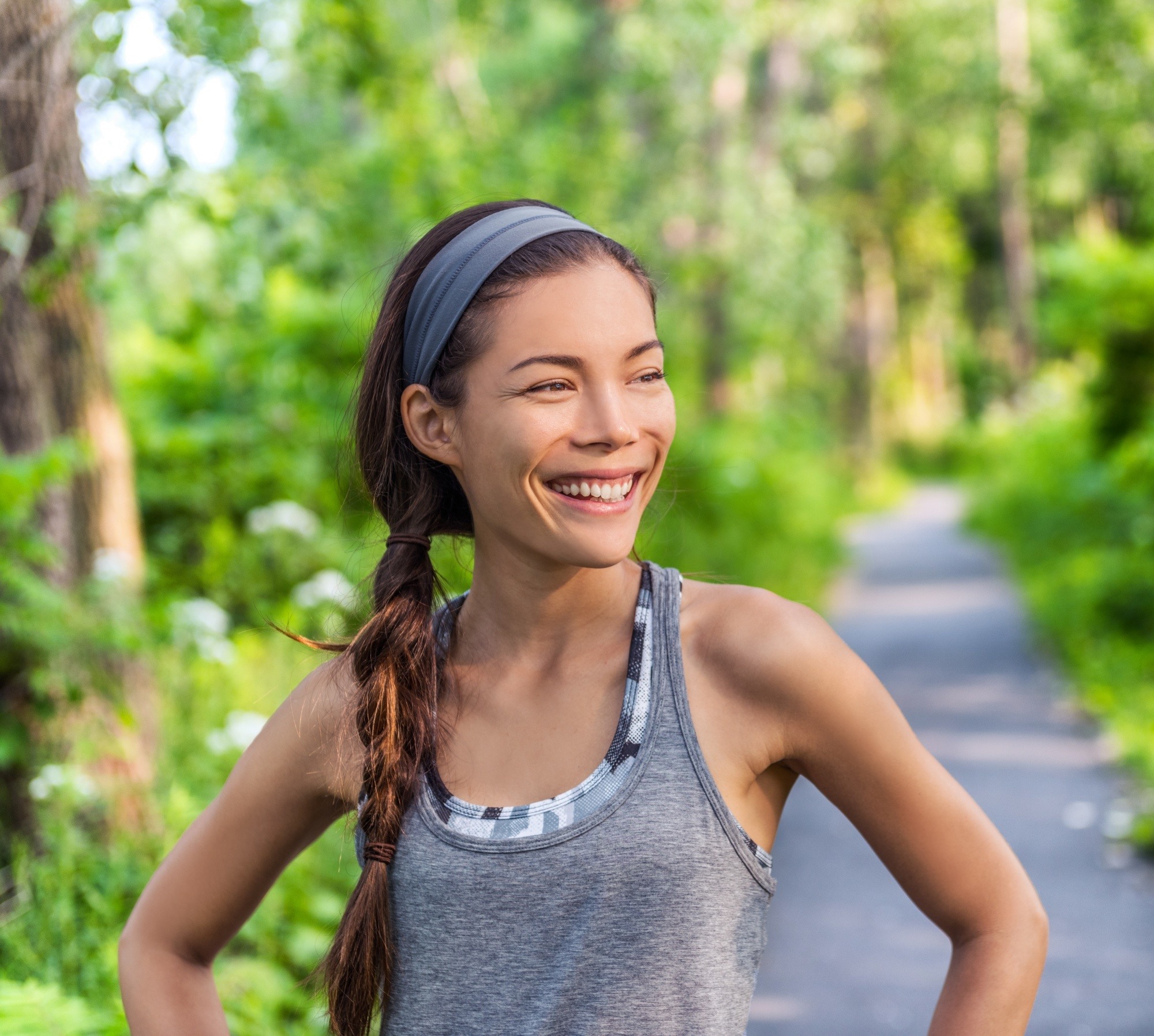 White hair causes: Asian woman with long brown braided hair wearing a gray headband and gray workout top outdoors