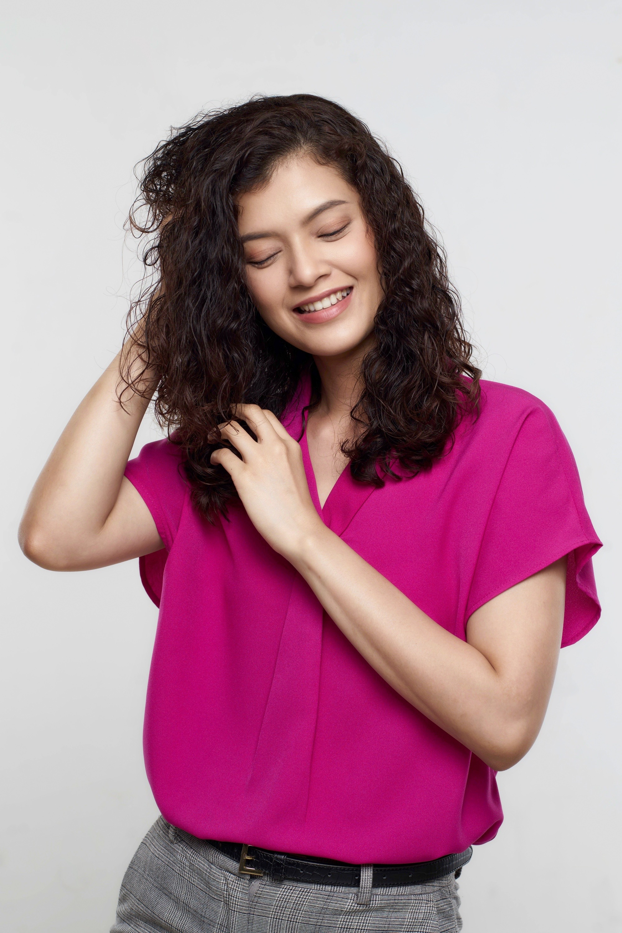 How to protect hair from pollution: Asian woman touching her curly dark hair and smiling