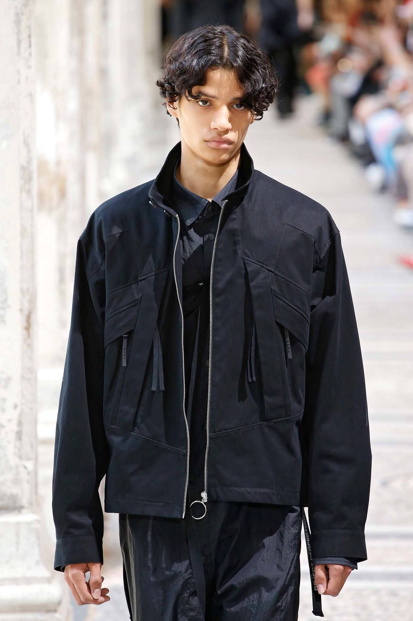 Male model with curly hair wearing a Đen jacket on the runway 