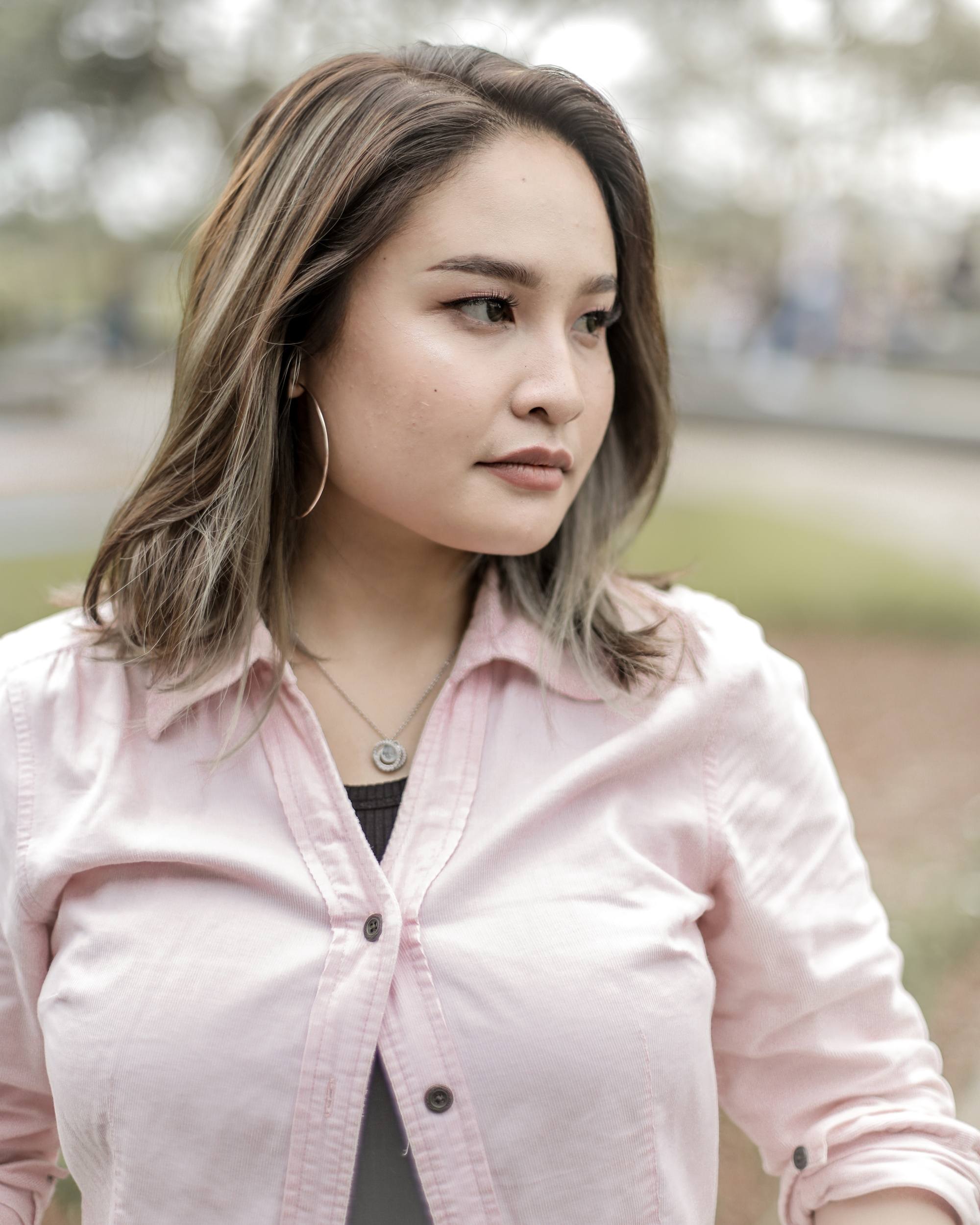 Asian woman with ash brown medium length hair wearing a pink blouse outdoors