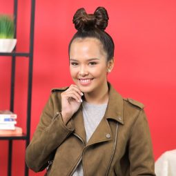 Asian woman with a bow style updo wearing a jacket standing against a red wall
