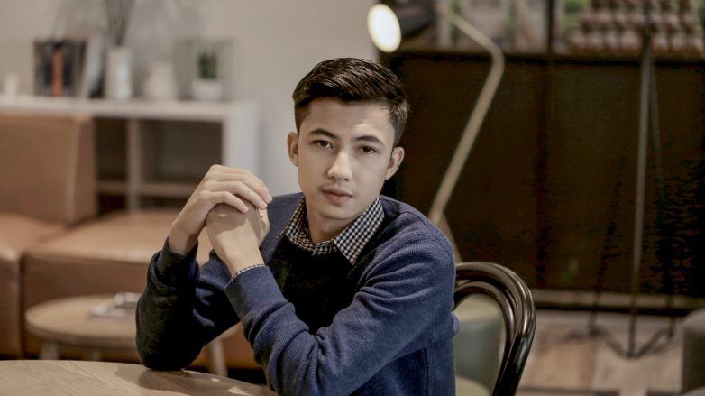 Asian man with an easy comb over hairstyle for men wearing a blue sweater and sitting in an office