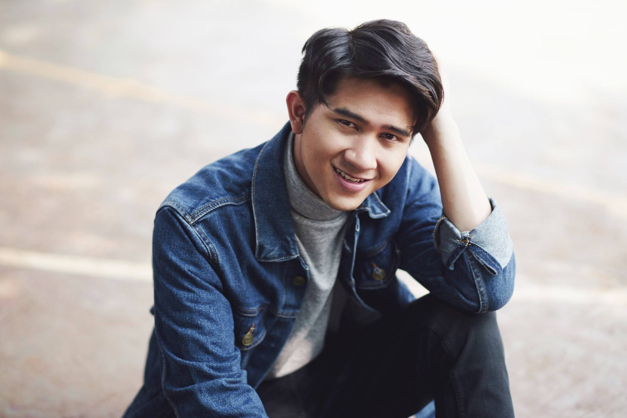 Asian guy look shyly at the camera wearing a blue denim jacket and one of the korean wavy hairstyles for men