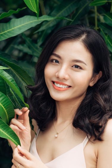 Naturals range discounts: Asian woman with dark wavy hair smiling with leaves in the background