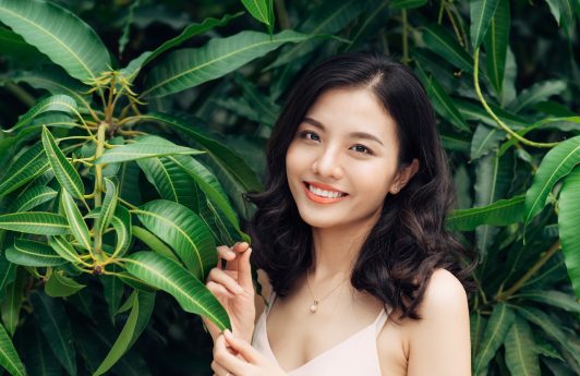 Naturals range discounts: Asian woman with dark wavy hair smiling with leaves in the background