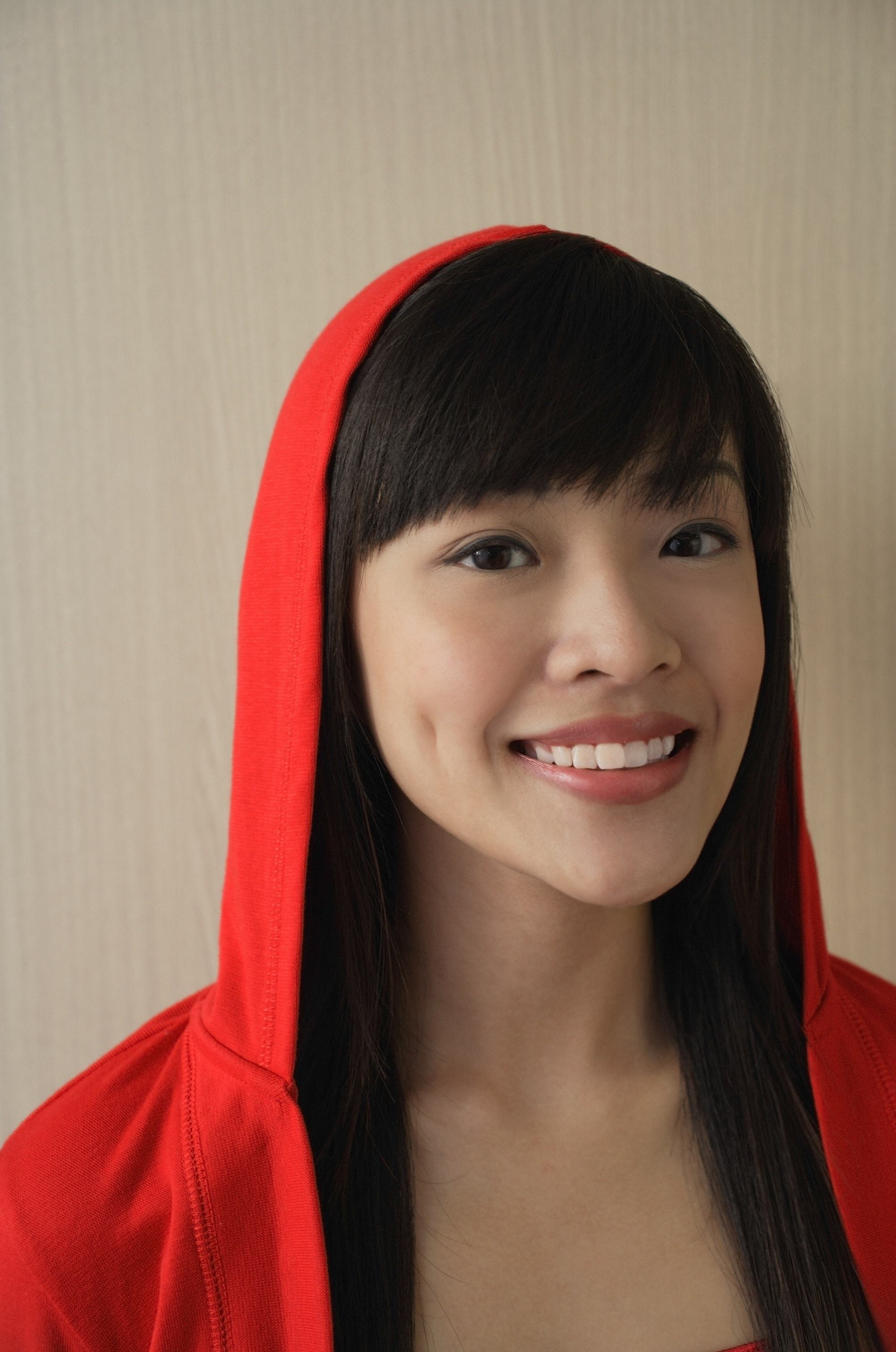 Asian woman with black hair and wispy bangs, wearing a red hoodie