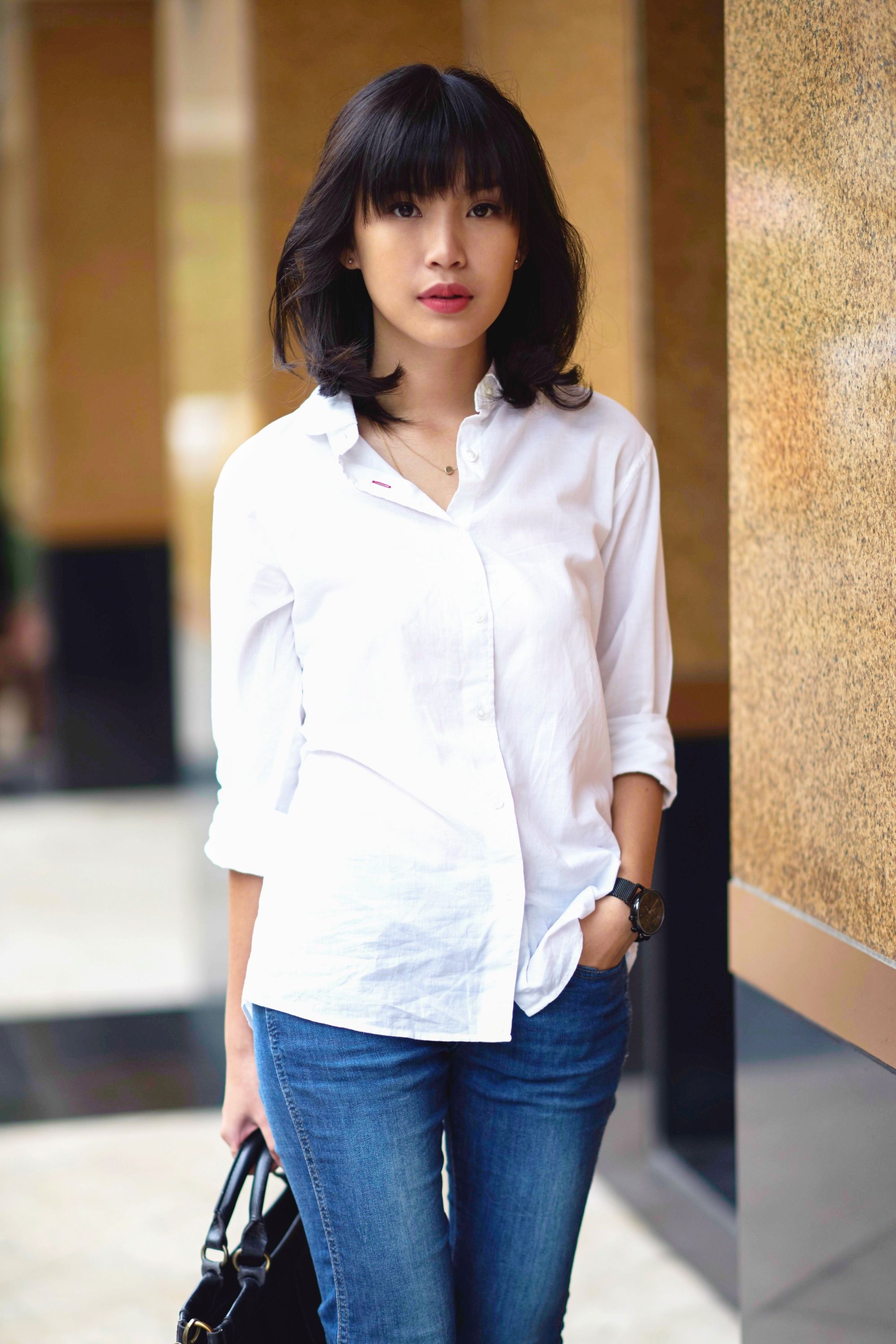 Femme asiatique avec un long carré agité avec une frange portant un chemisier blanc et un jean en denim