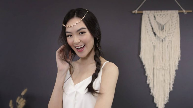 Asian woman with messy side braid with headband smiling at the camera