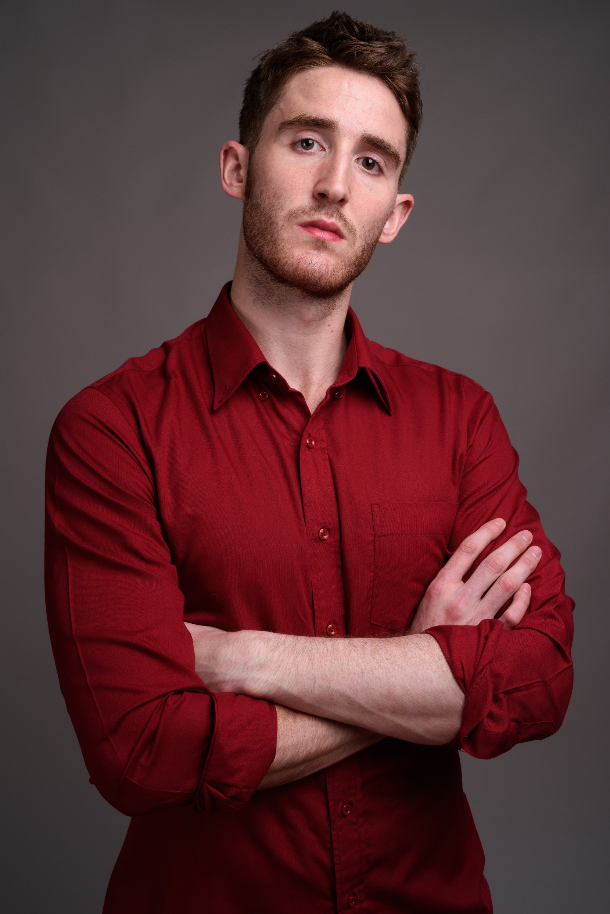 Haircuts for men with thick hair: a Caucasian man with an angular brushed up hairstyle, wearing a red long-sleeved button down shirt with his arms crossed