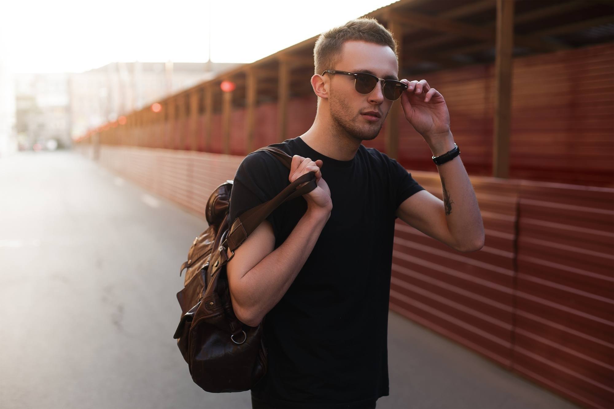 Haircuts for men with thick hair: a Caucasian man in a black shirt and shades with a shaggy brush cut while holding a bag
