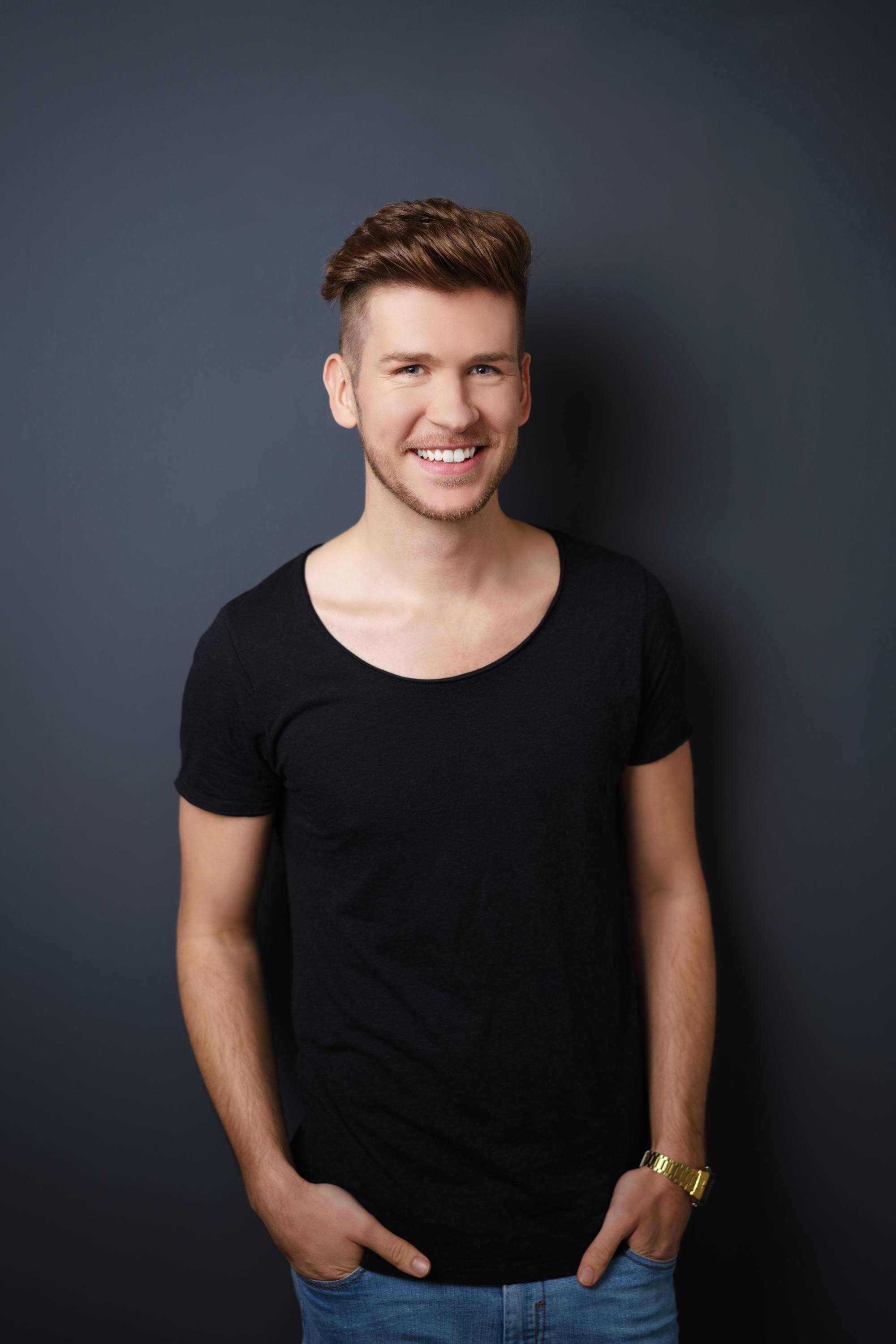 Haircuts for men with thick hair: Caucasian man in a black shirt smiling with his thick quiff undercut hairstyle