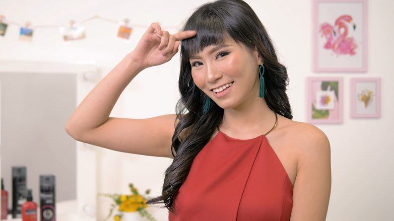 Asian woman with long wavy hair and baby bangs wearing a halter top smiling