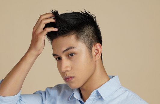 Asian man wearing a blue polo touching his hair to show itchy scalp causes