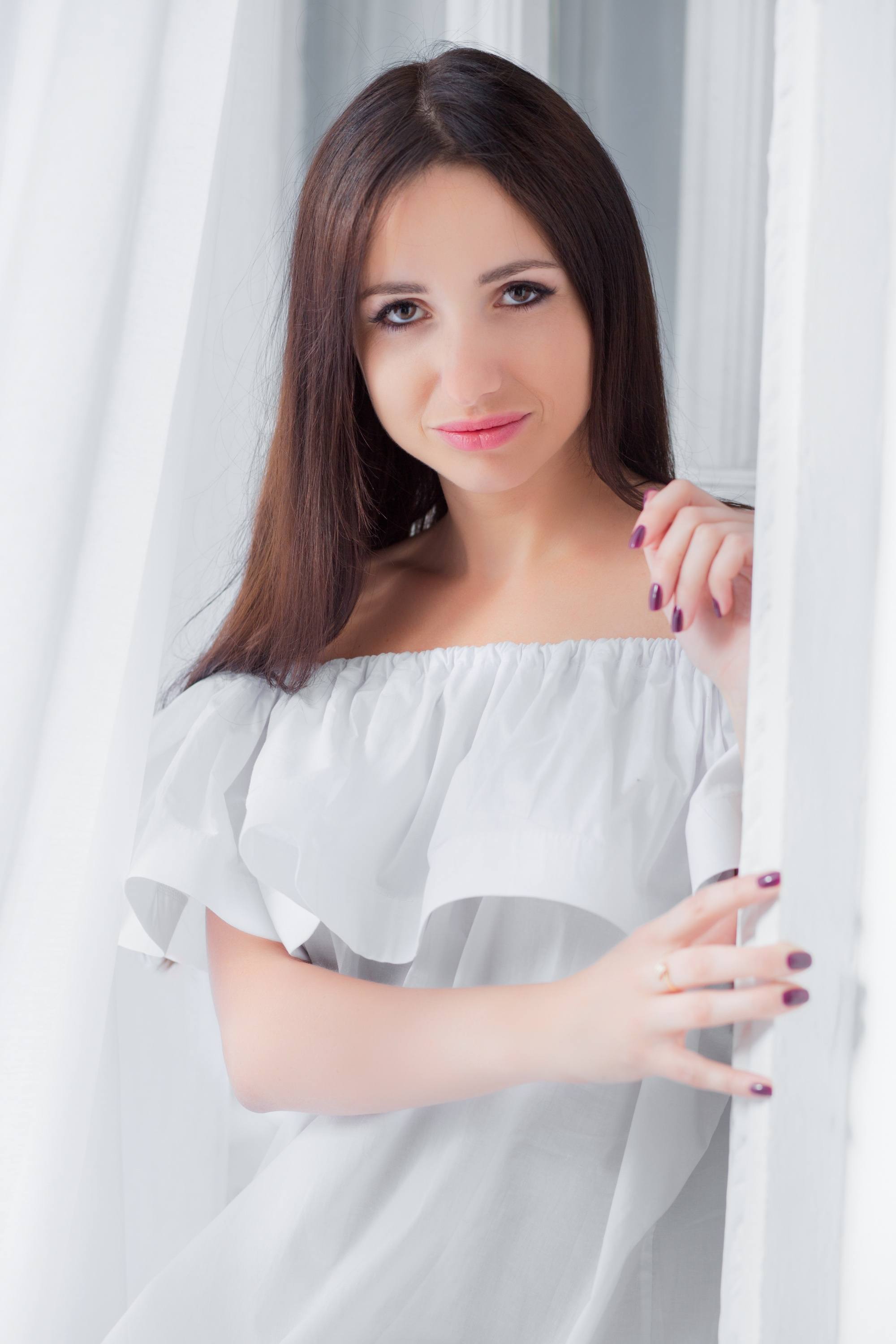 Woman with long straight dark brown hair wearing a whilte off-shoulder top