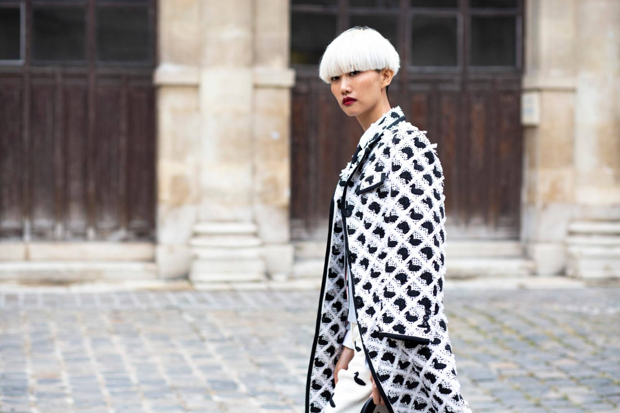 Woman with blonde bowl cut short hair wearing a checkered coat outdoors