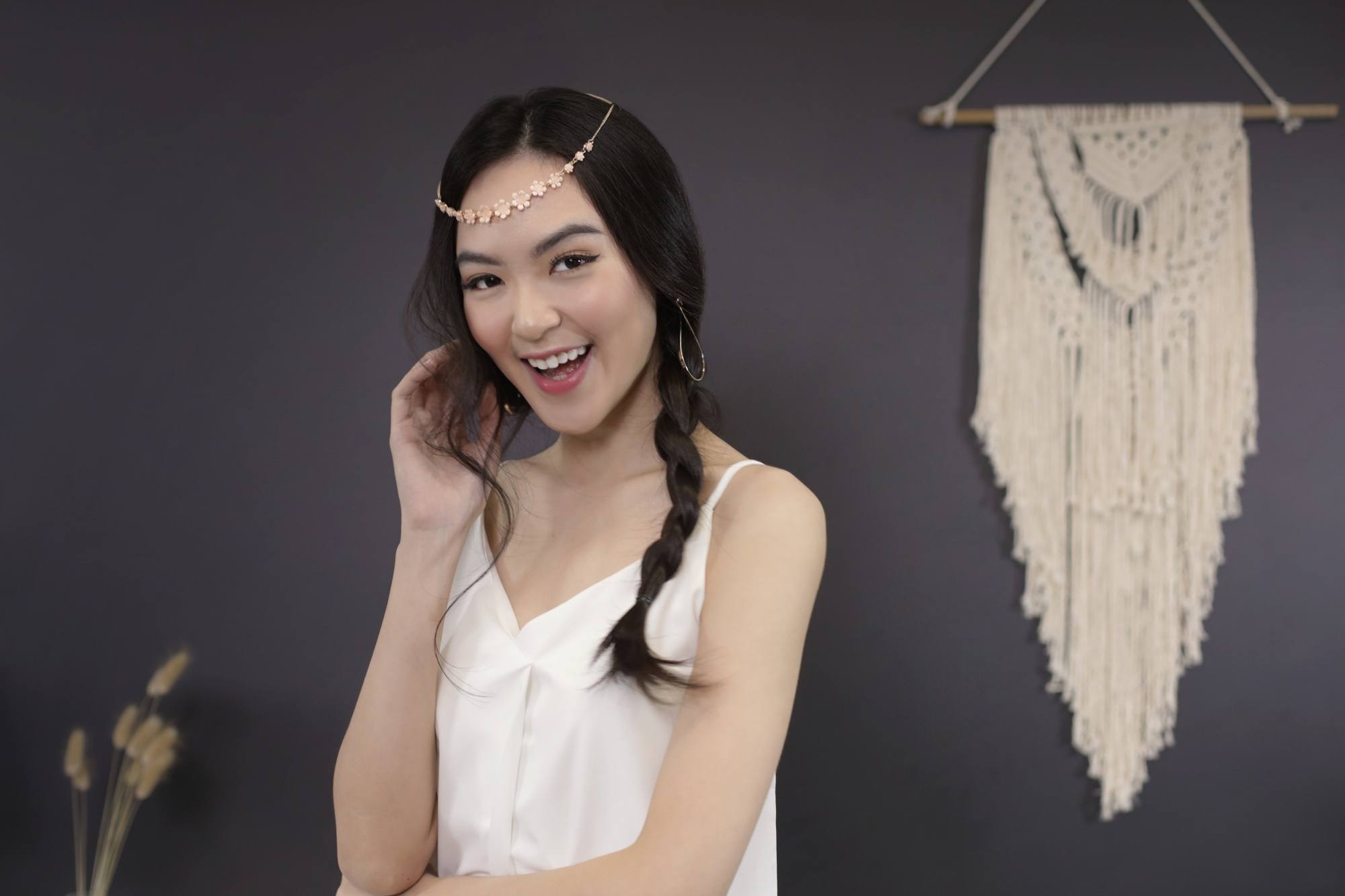 Heureuse femme asiatique avec une coiffure tressée sur le côté en désordre portant un haut sans manches blanc