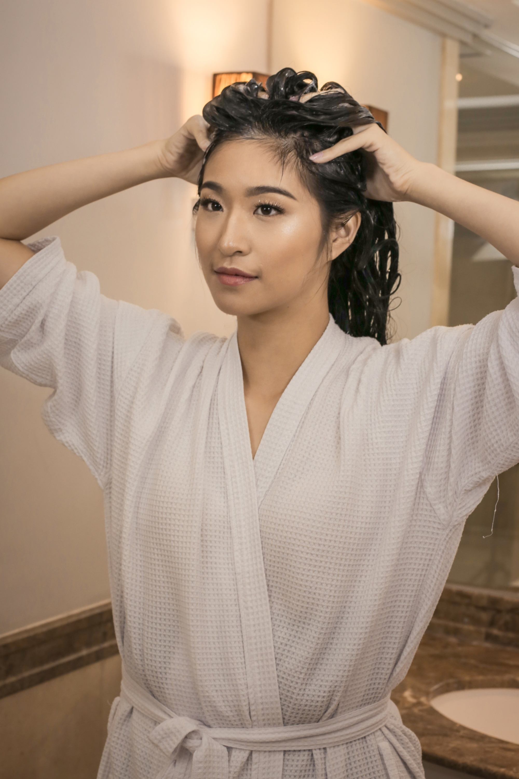 Asian woman wearing a white robe shampooing her long black hair