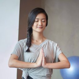 Asian woman doing yoga with long black hair in a fishtail braid and wearing a gray shirt