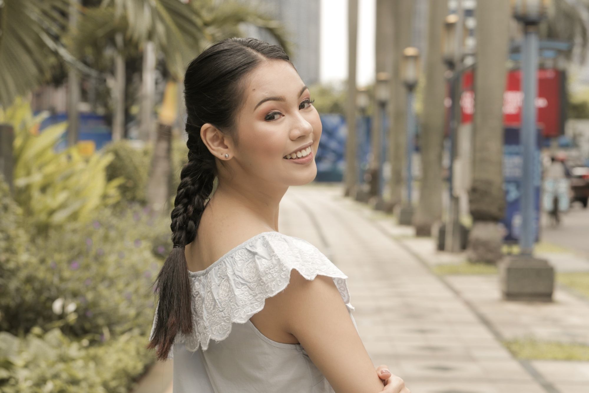 Asian woman with triple braid hairstyle wearing a ruffled top outdoors