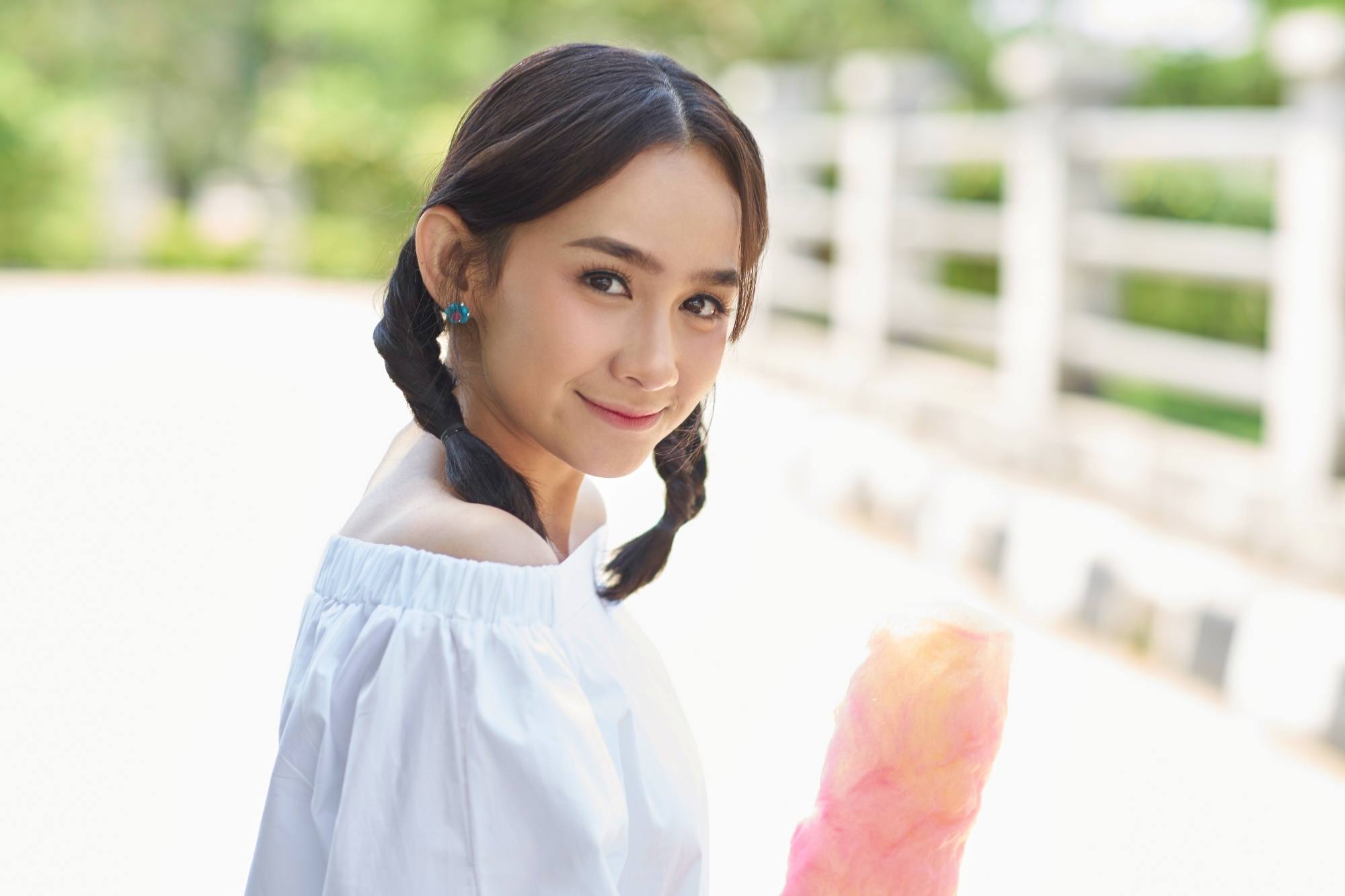 Asian woman with shoulder-length hair in twin fishtail braids smiling outdoors