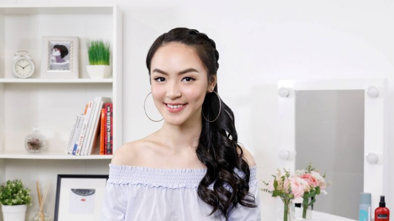 Asian woman with long hair in a side-swept Dutch braid wearing an off-shoulder blouse