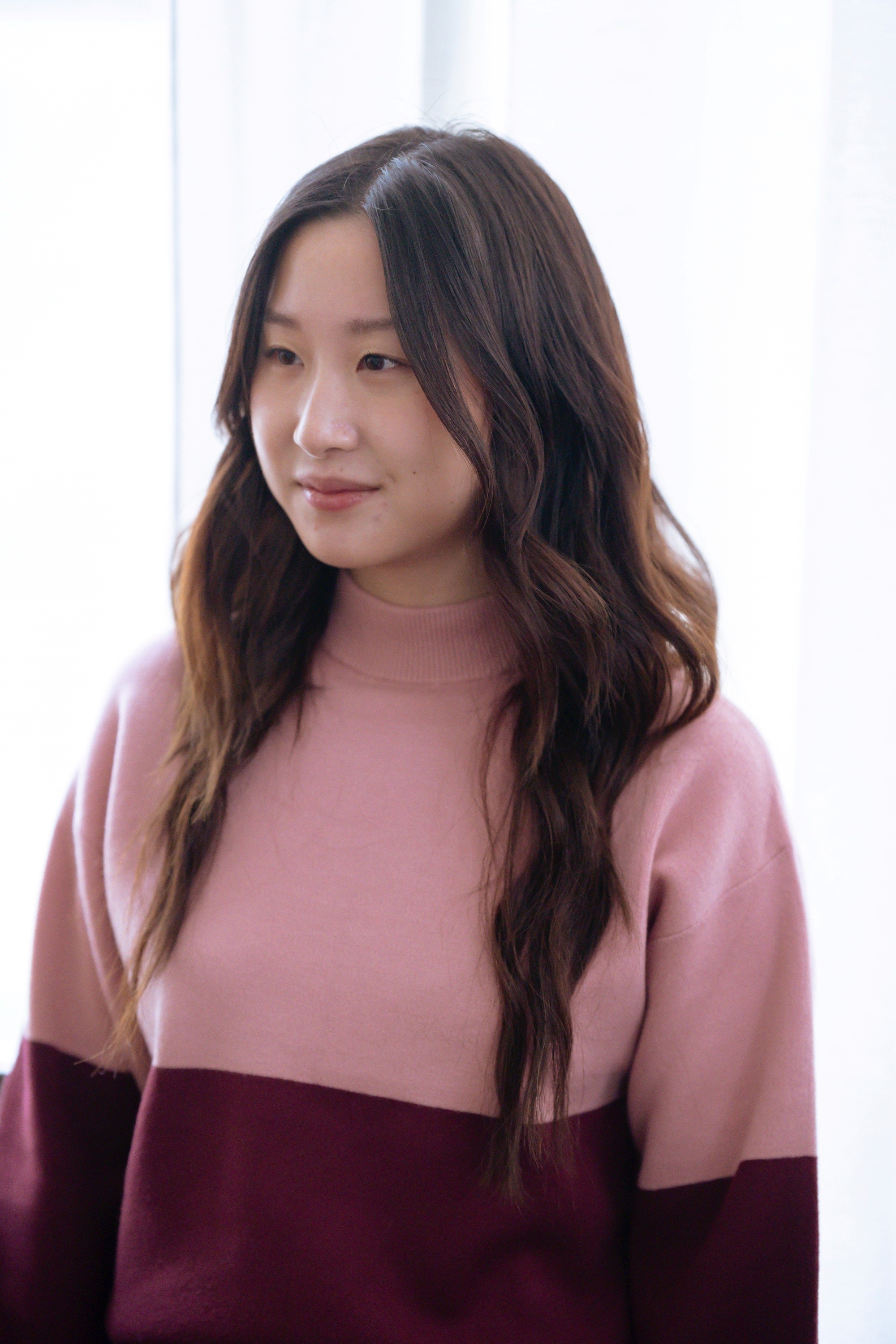 Asian woman with long beach waves wearing a pink sweater