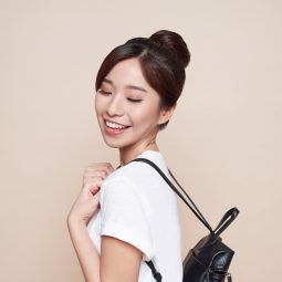 Asian woman with a hair donut wearing a white shirt carrying a black leather backpack