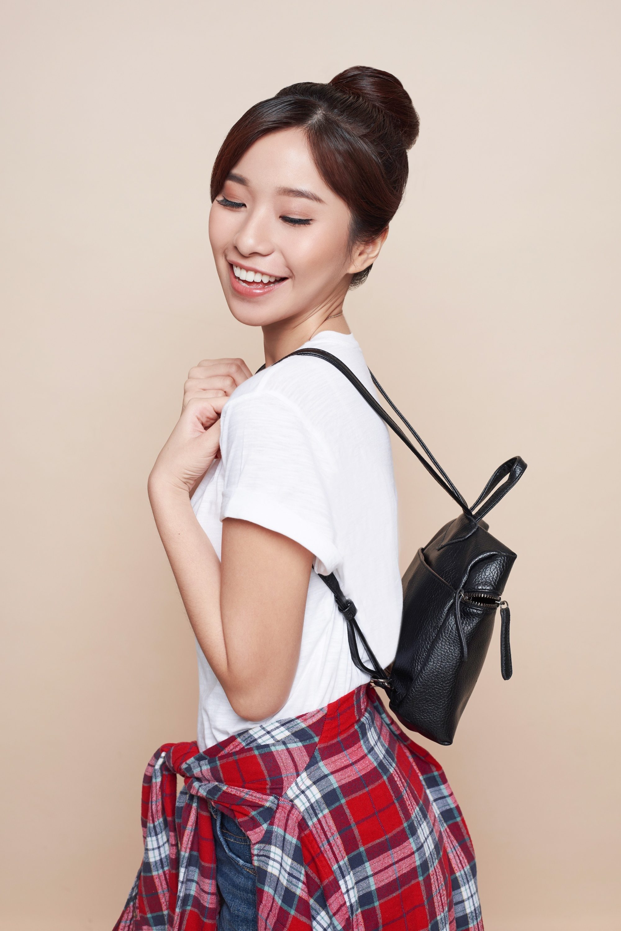 Asian woman with a hair donut wearing a white shirt carrying a black leather backpack