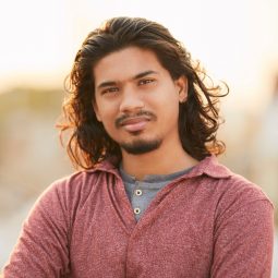 Asian man with long wavy hair wearing a sweater outdoors