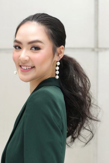 Asian woman with tousled ponytail wearing a dark green blouse