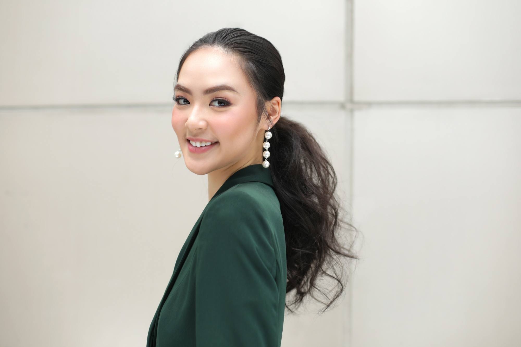 Asian woman with tousled ponytail wearing a dark green blouse