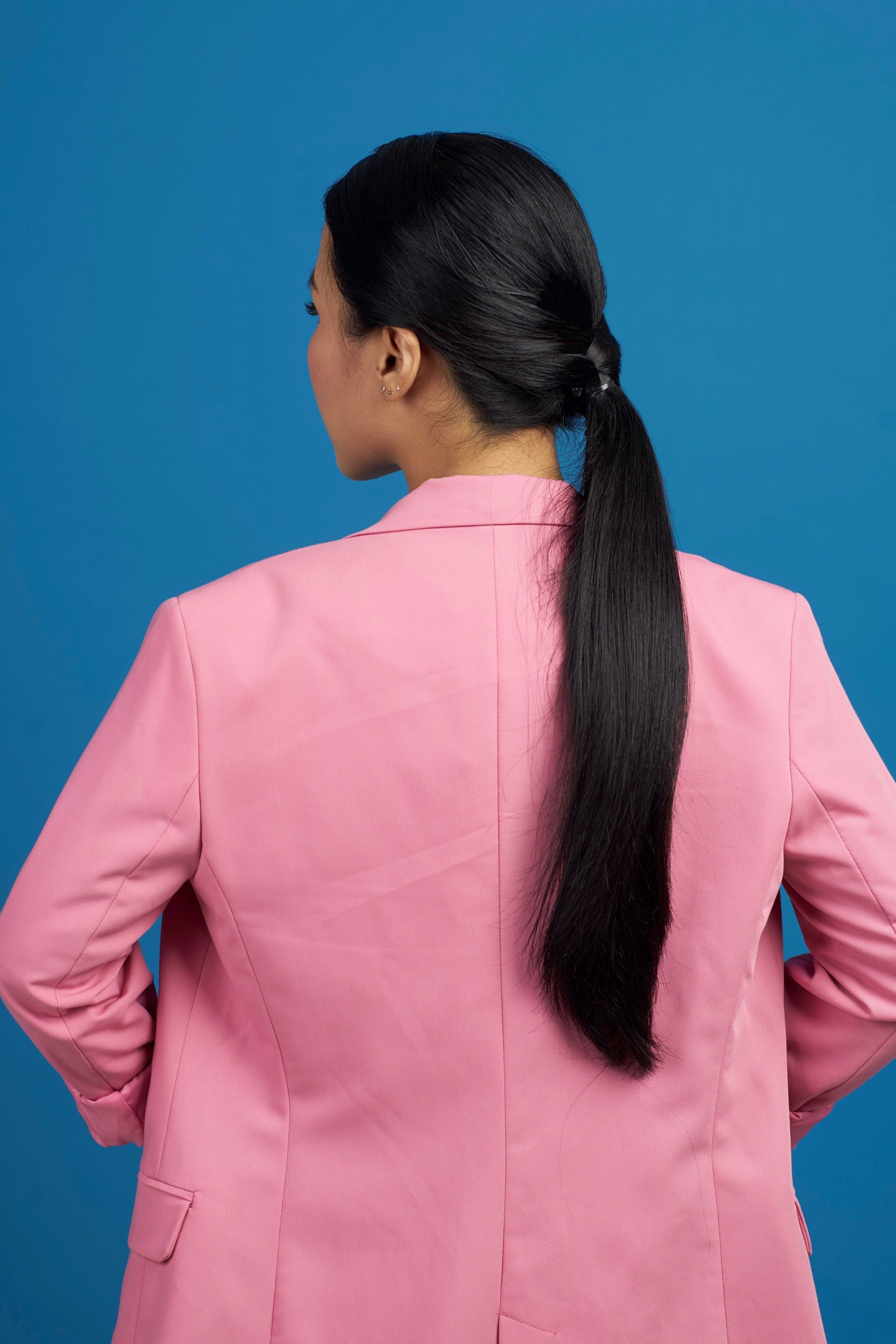 Back shot of an Asian woman with long black hair wearing a pink suitwi