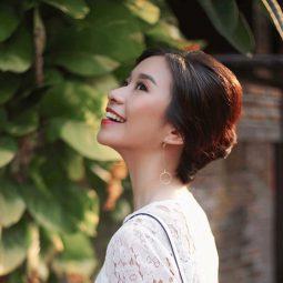 Side view of an Asian woman with hair in a French twist wearing a white dress outdoors