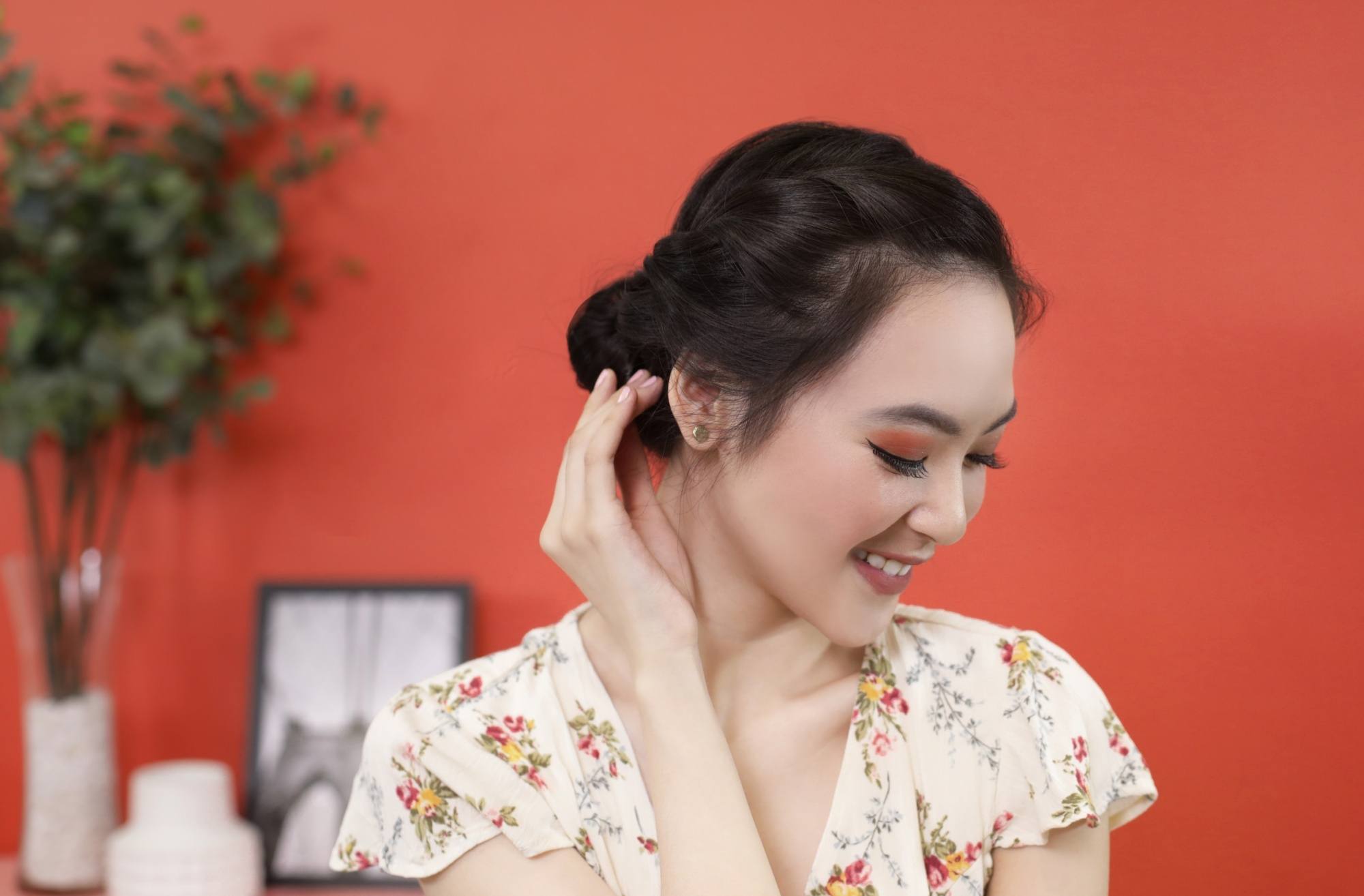 Closeup shot of an Asian woman with french rope braid bun hairstyle wearing a floral dress against an orange wall