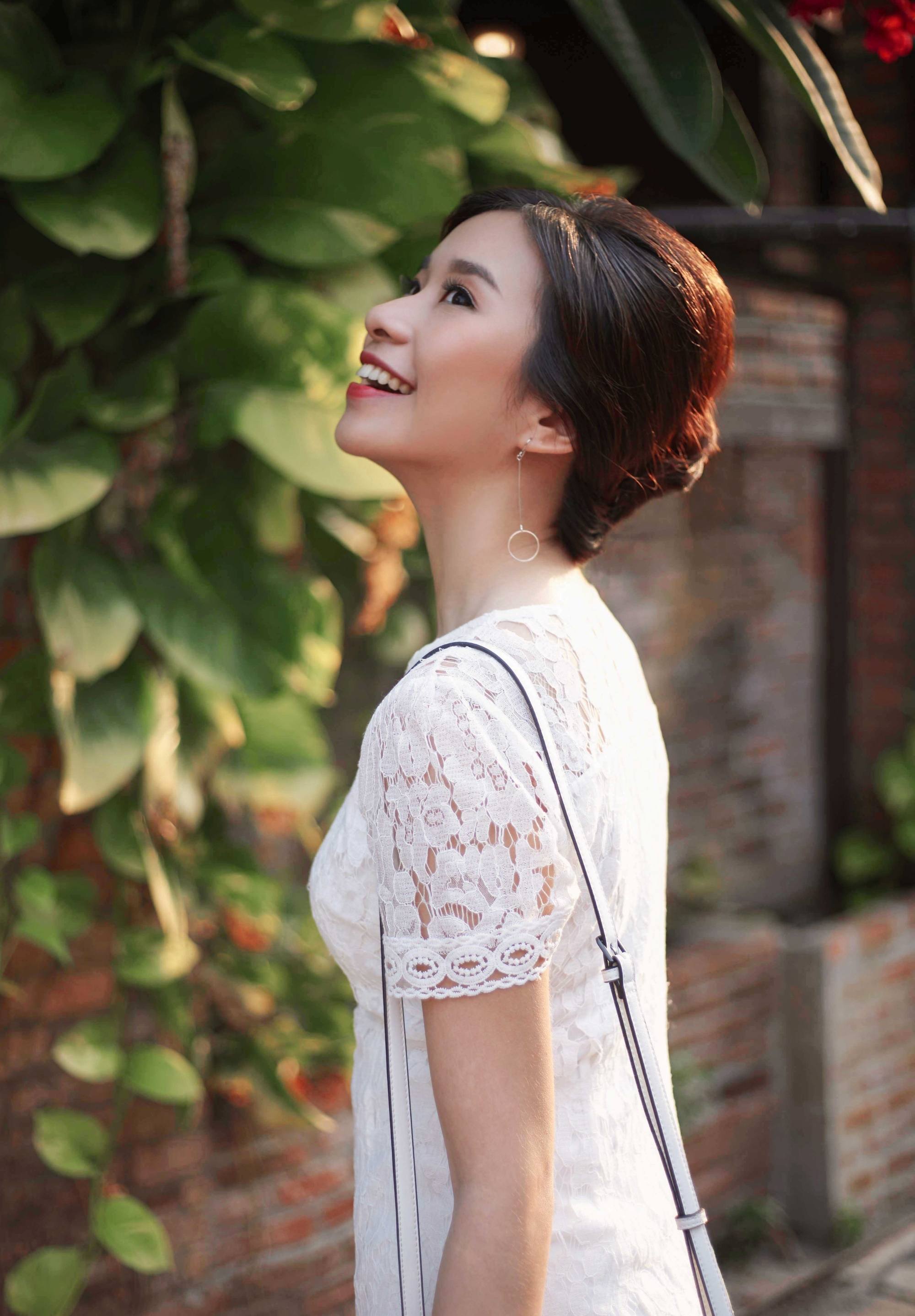 Side view of an Asian woman with hair in a French twist wearing a white dress outdoors
