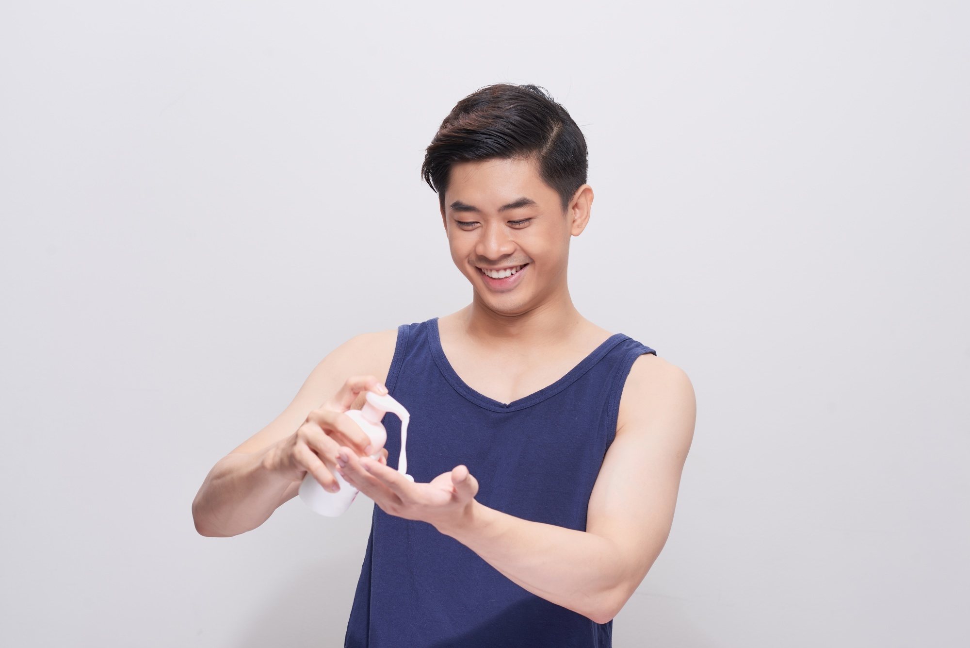 Asian man wearing a blue tank top putting shampoo on his hand