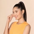 Asian woman with long black hair in a high ponytail wearing a mustard-colored dress