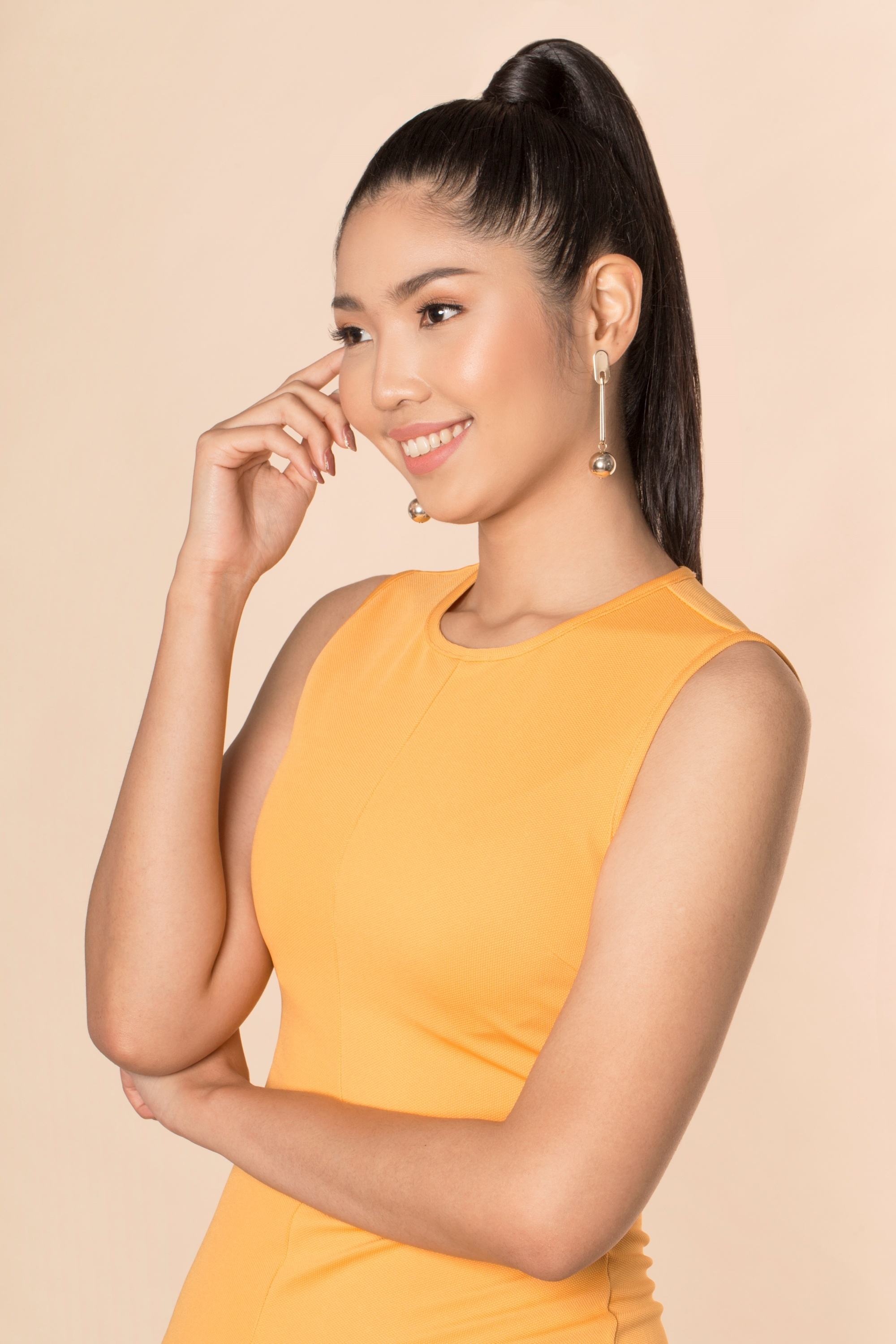 Asian woman with long black hair in a high ponytail wearing a mustard-colored dress