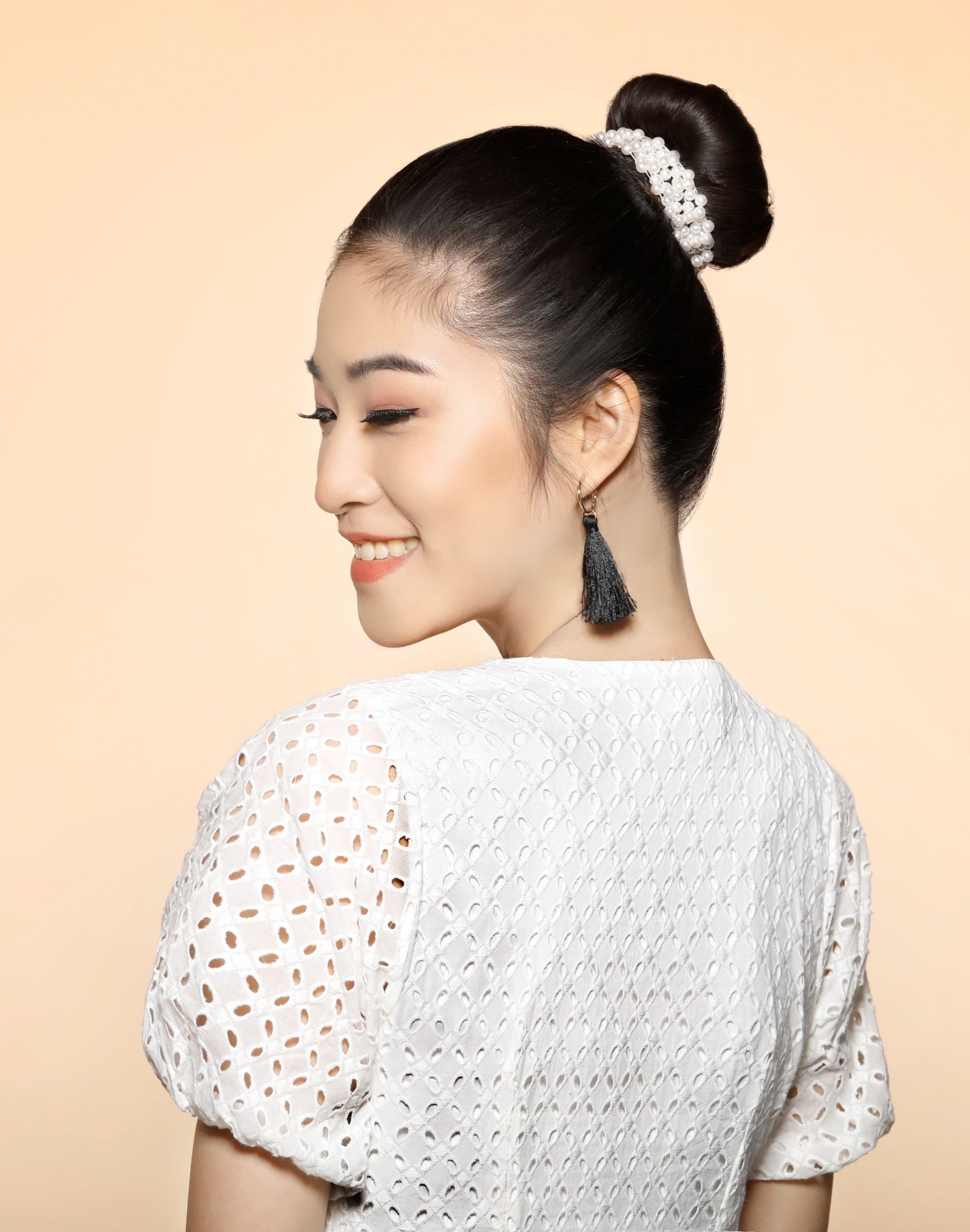 Asian woman with a top bun hairstyle wearing a white dress and black dangling earrings