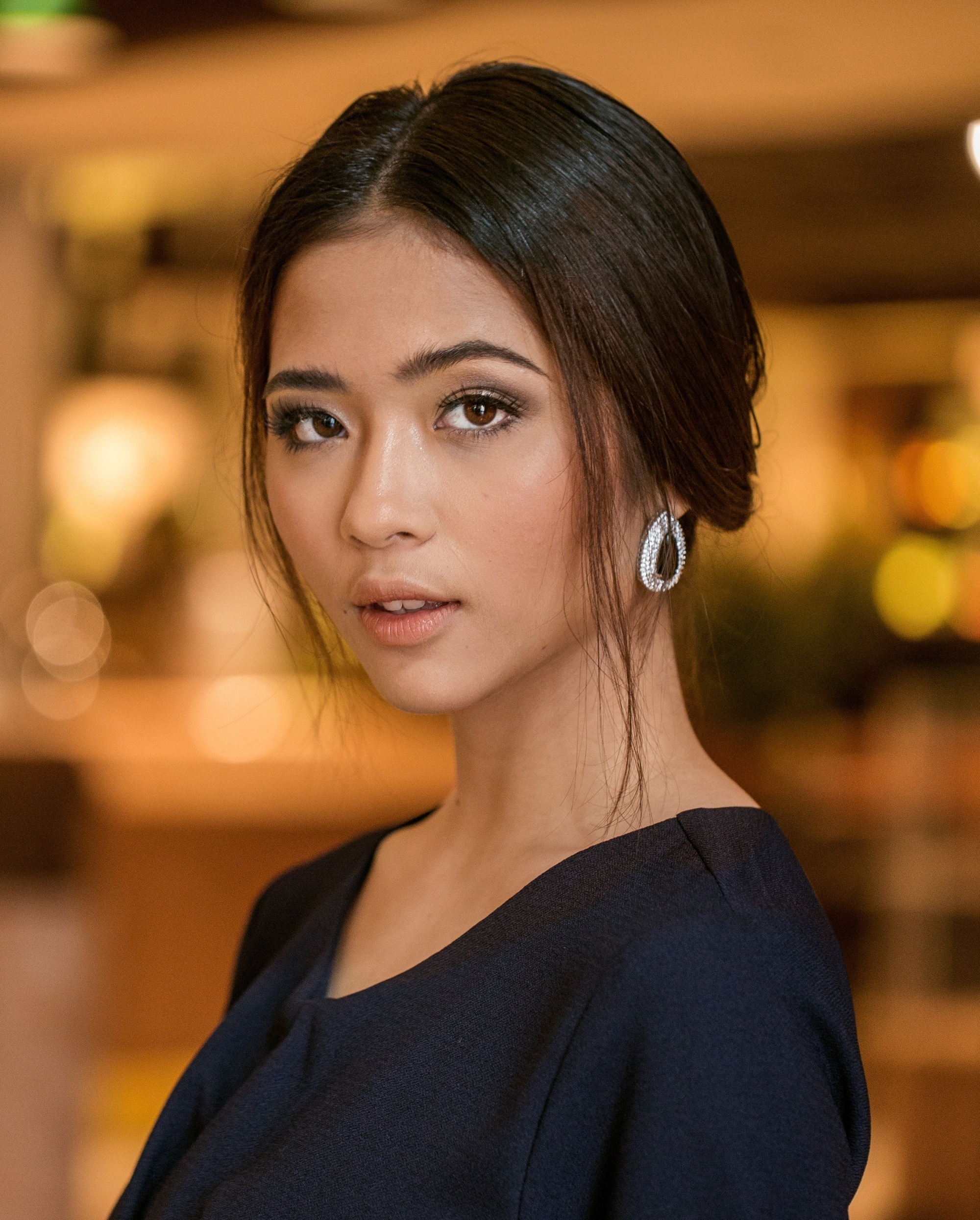 Asian woman with an updo hairstyle wearing a dark blue dress and earrings