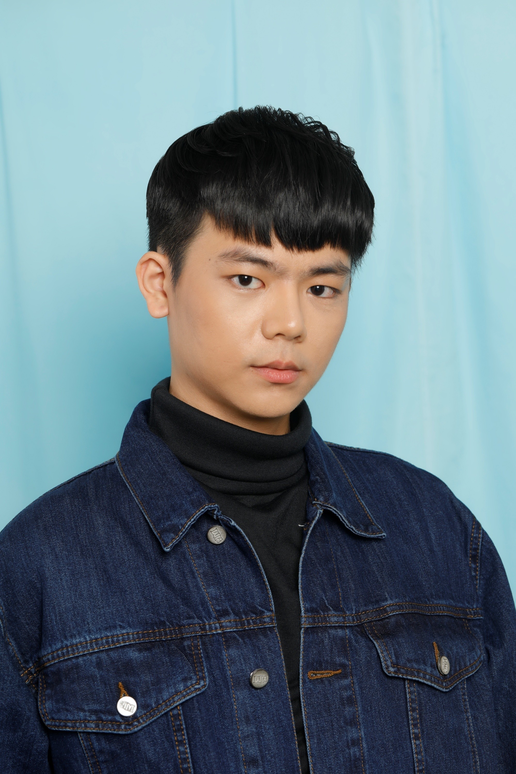 Asian man with a two-block haircut wearing a dark shirt and denim jacket