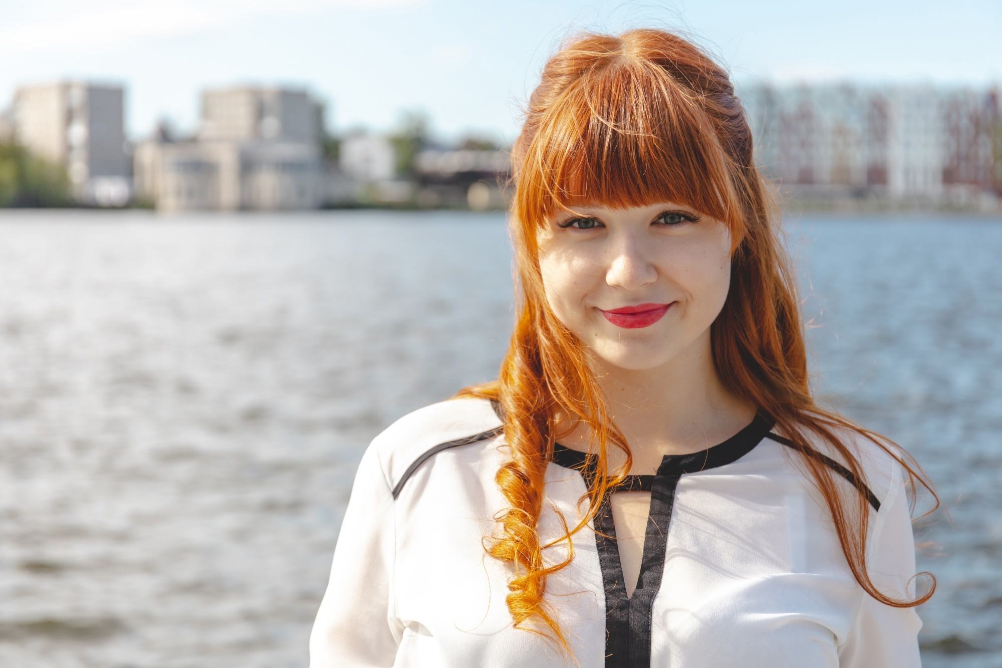 Woman with red curly hair with bangs smiling near the sea