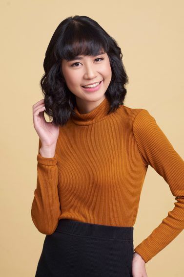 Asian woman with wavy lob and blunt bangs wearing a brown top and black skirt