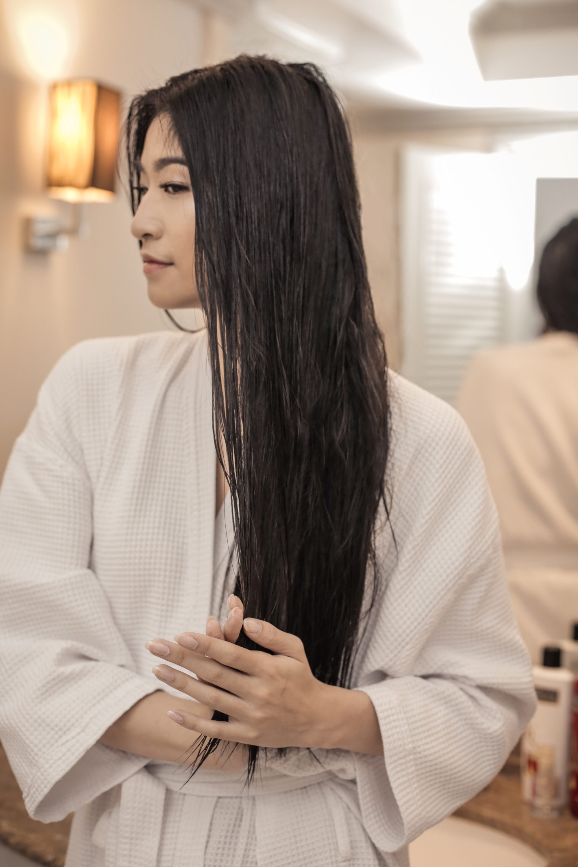 Dry and Damaged hair: Asian woman wearing a white bathrobe shampooing her hair