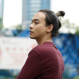 Messy hair bun: Asian man with a samurai bun wearing a maroon long-sleeved shirt