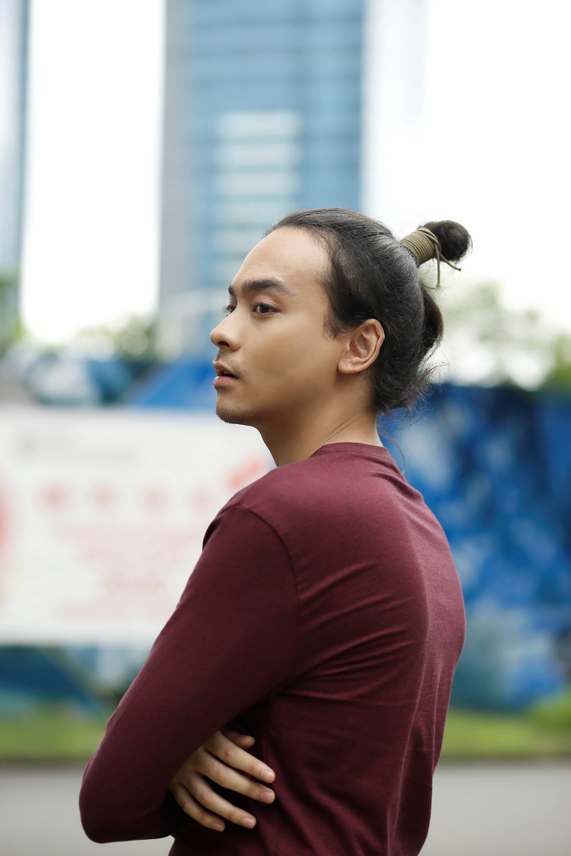 Messy hair bun: Asian man with a samurai bun wearing a maroon long-sleeved shirt