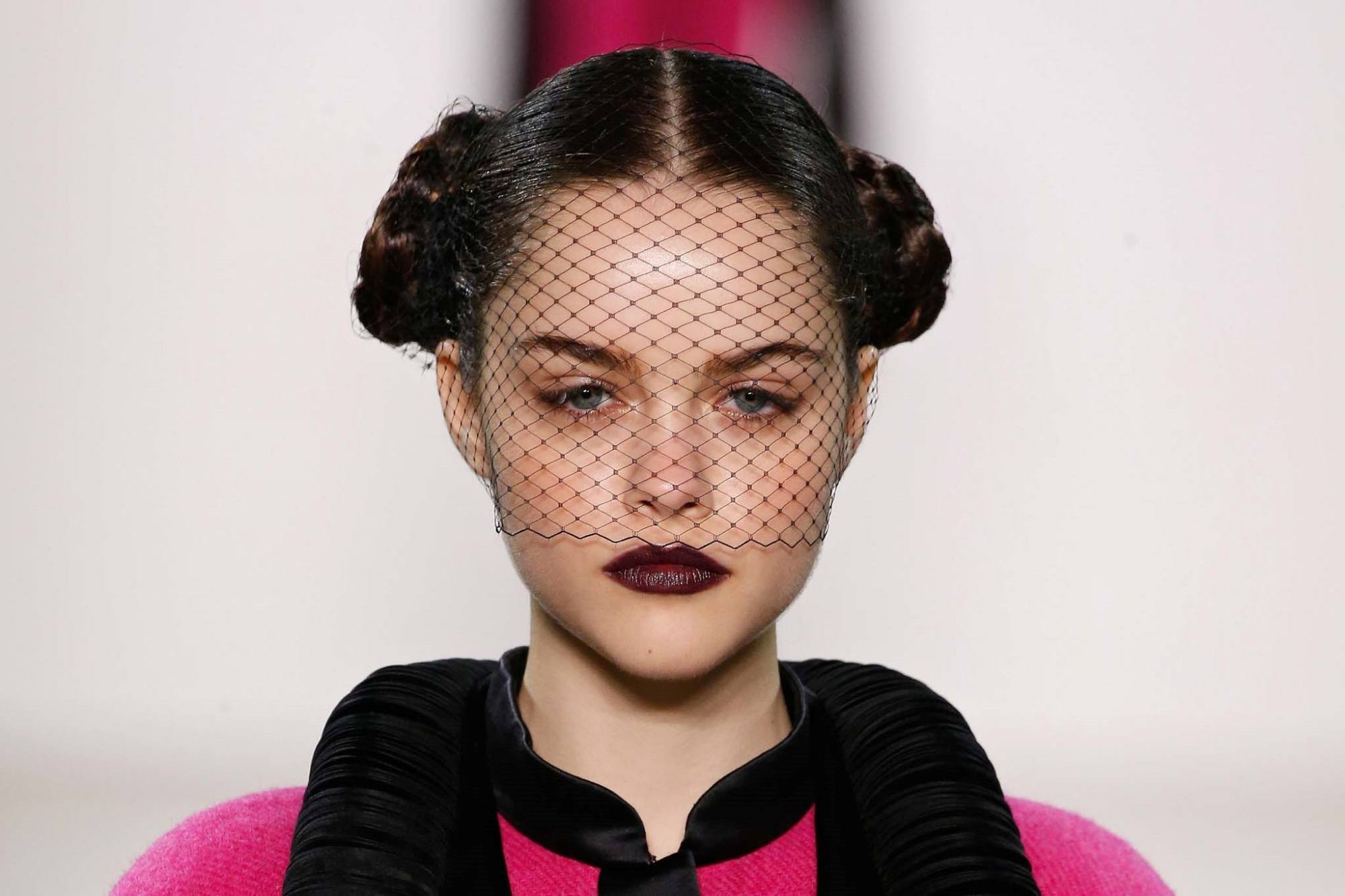 Model with a double bun hairstyle wearing a pink dress on the runway