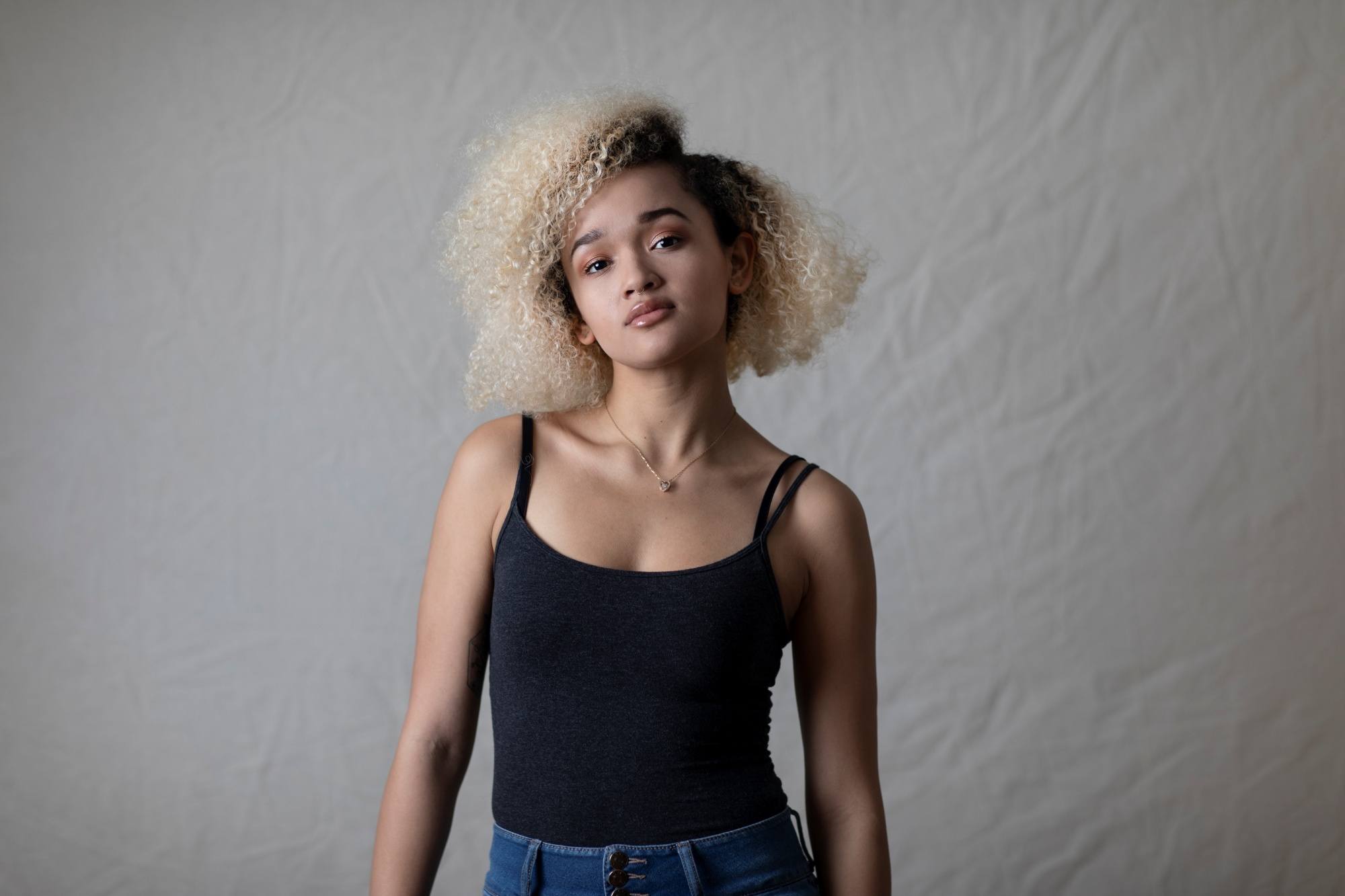 Asian woman with blonde curly hair wearing a black tank top