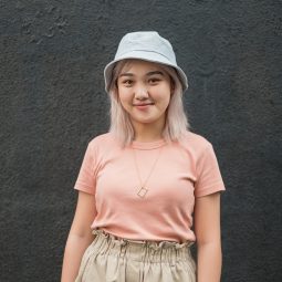 Self expression: Asian girl with platinum-colored hair is wearing a hat while standing against a black background