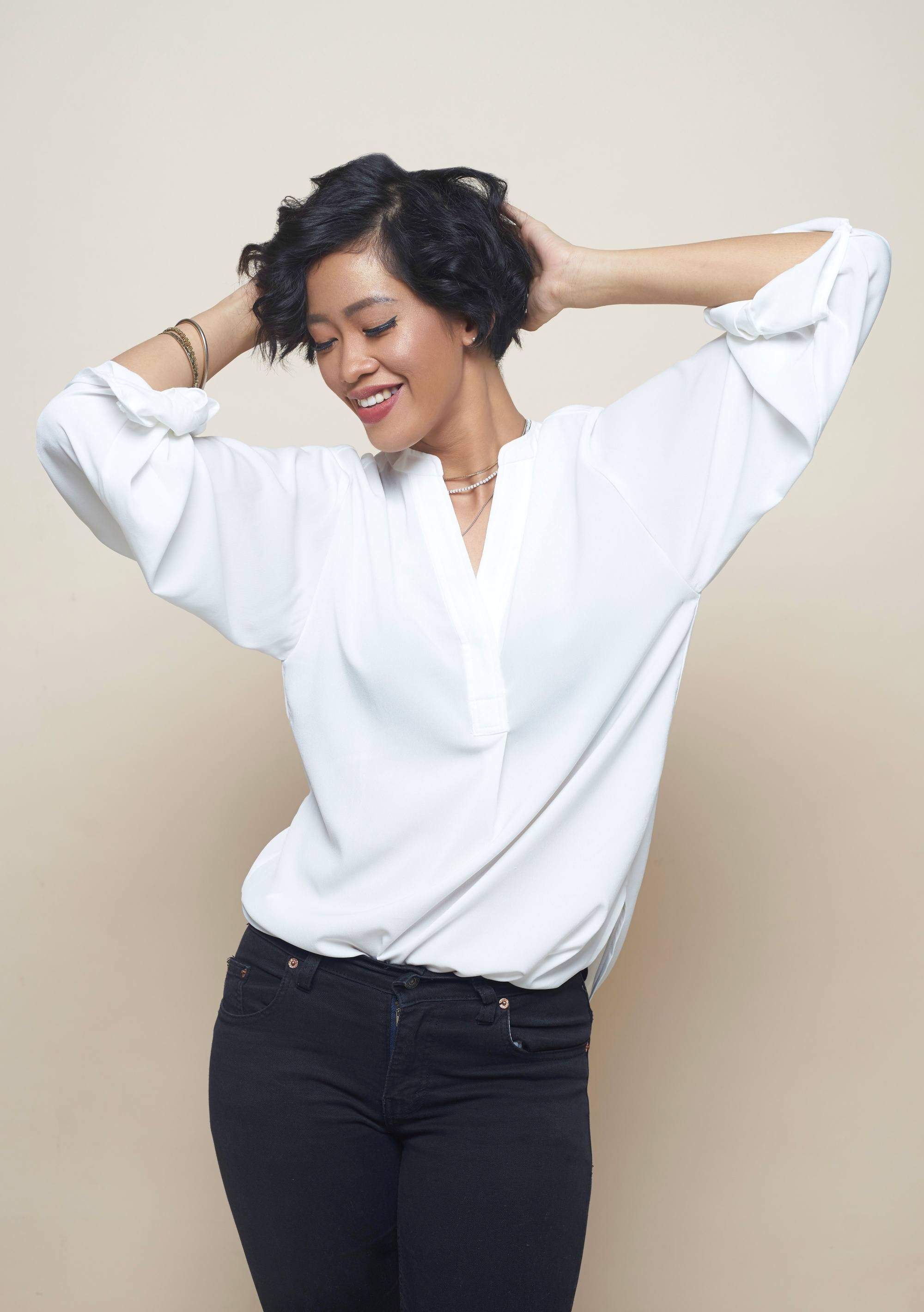 Haircuts for curly hair: Asian woman with curly short hair wearing a white blouse and black pants